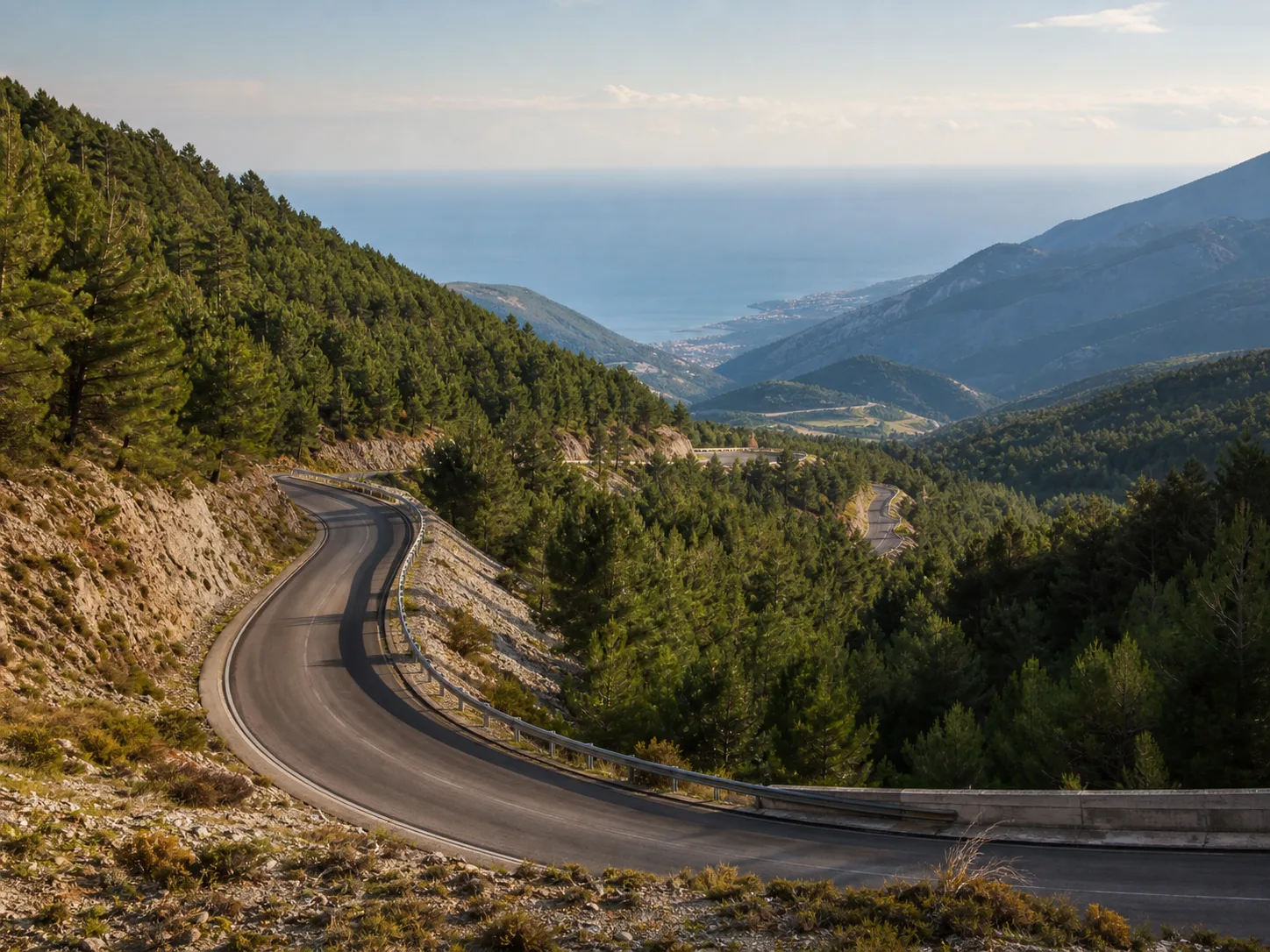 Mountain road curving through forest under shifting alpine cloud.