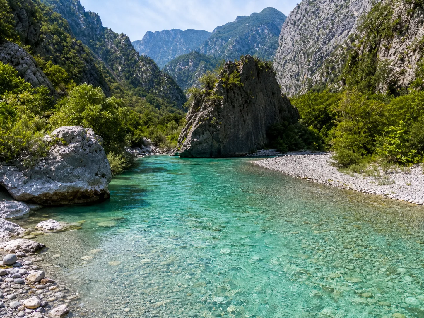Clear river with bright turquoise water between rugged mountain slopes.